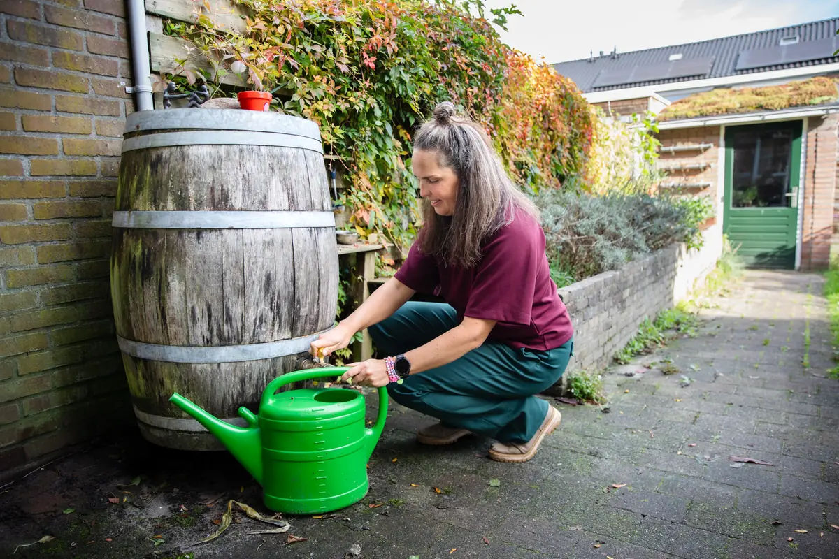 Natasja vult een gieter met regenwater uit de regenton in haar tuin